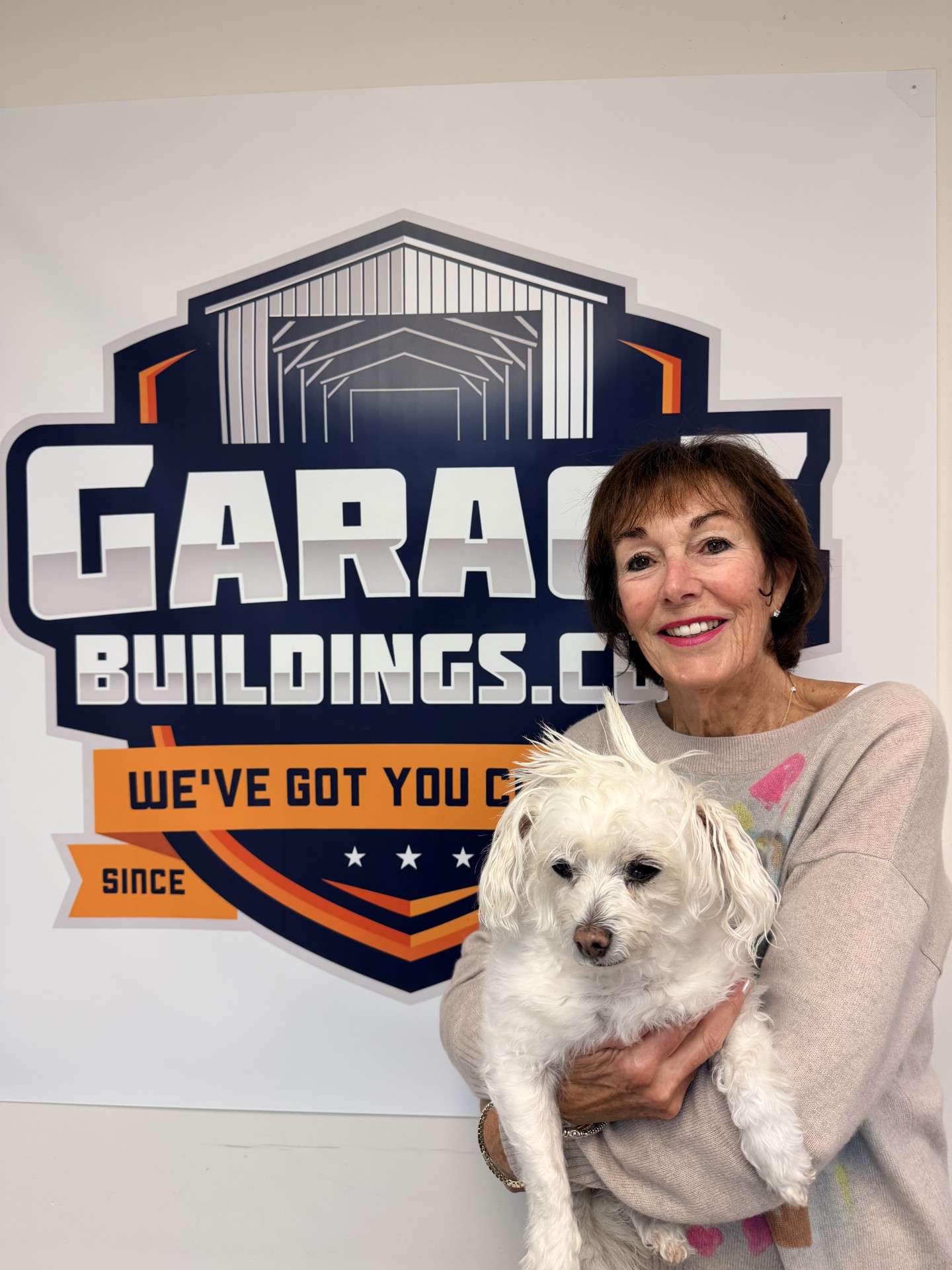 A Garage Buildings team member holding the office dog in front of the company logo