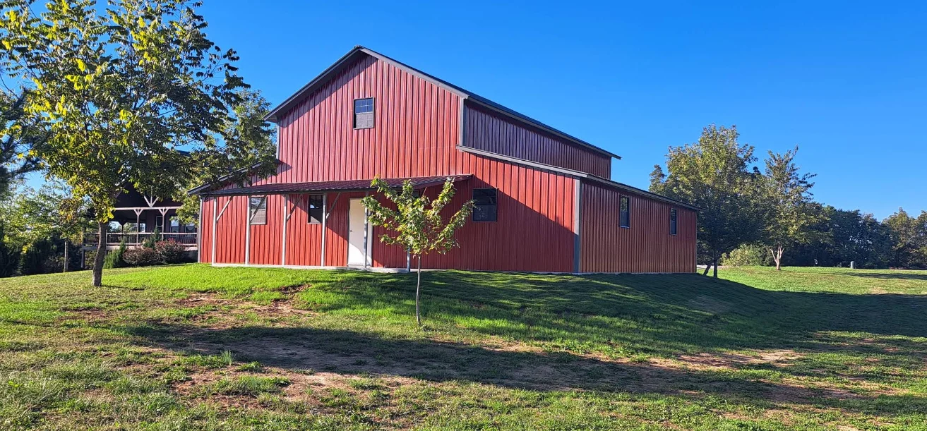 Red barn-style building surrounded by green grass and trees under a clear blue sky
