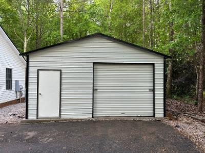 Metal garage with one large roll-up door and a side entrance in a wooded area